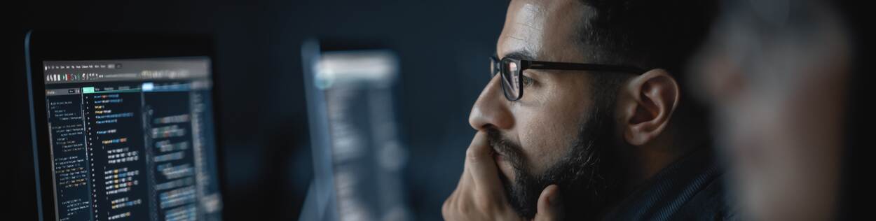 Man met kort haar en een bril bekijkt ontwikkelaarscode achter zijn computer