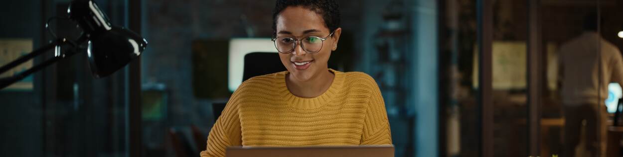 Vrouw met donker haar en een bril werkt achter haar laptop